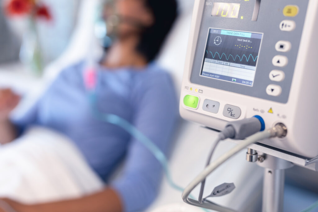 Ventilator monitor and female patient in hospital bed with oxygen ventilator